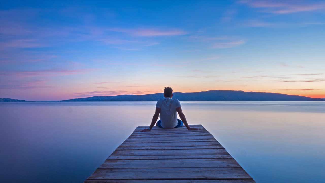 man sitting calmly looking at still water...at sunrise